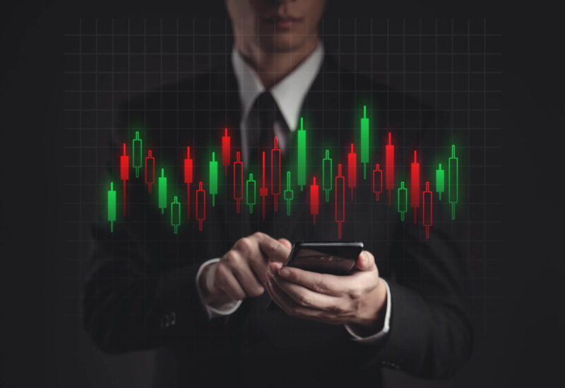 Businessman in black suit using smartphone planning for investment. Showing candlestick chart hologram technology.